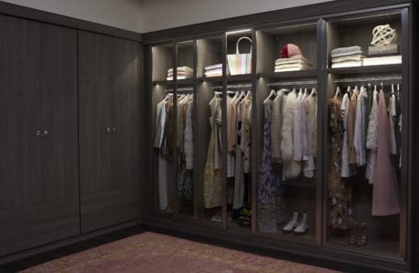Dark brown wardrobe close with walk in closet with rods, shelving, and built in lighting created by California Closets