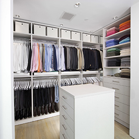 Walk in Closet with custom shelving, drawers, closet rods and island dresser in a white wood grain finish by California Closets