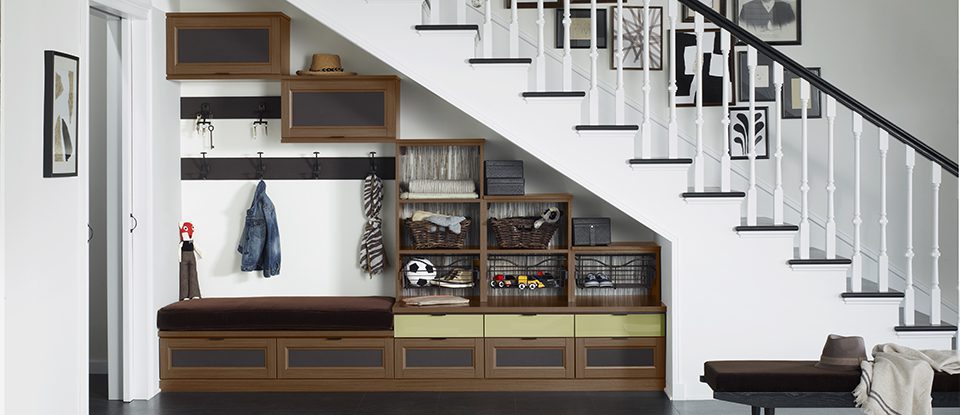 Under the stairs storage closet in an entry in a dark wood grain finish with hooks, cubbies, bench and cabinets