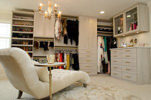 Mottled White Walk in Closet with Lounge Chair Shelving Cabinets and Gold Accented Closet Rods and Handles