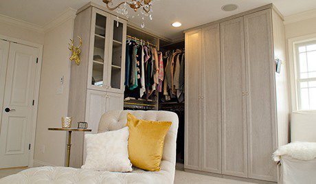 Mottled White Walk in Closet with Lounge Chair Shelving Cabinets and Gold Accented Closet Rods and Handles