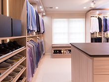 Light Wood Walk in Closet with Shoe Racks Hanging Clothes Built in Lighting and Stand Alone Dresser With Dark Brown Top