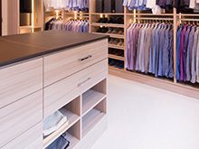 Light Wood Walk in Closet with Shoe Racks Hanging Clothes Built in Lighting and Stand Alone Dresser With Dark Brown Top