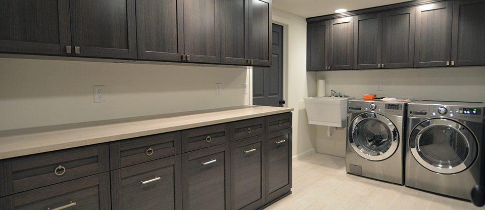 Dark Brown Wood Grain Laundry Storage Cabinets with Light Wood Counter Top and Stainless Steel Washer and Dryer