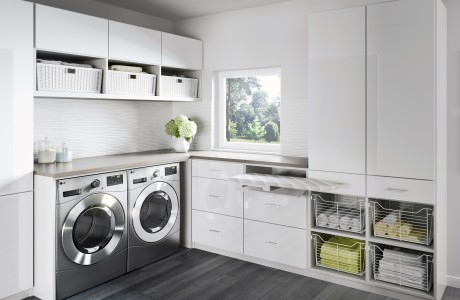 High gloss finish in all white laundry room with storage cabinets, drawers and baskets and a foldout ironing board by California Closets