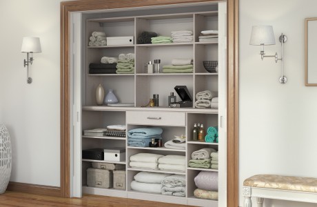 Wooden linen cabinet storage in an off white wood grain finish with custom shelving and a custom drawer by California Closets