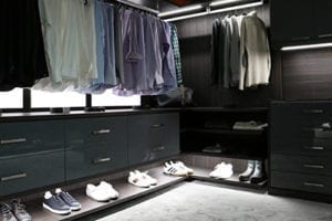Black Walk in Closet with High Gloss Cabinets and Drawers Built in Lighting and Wood Grain Backing