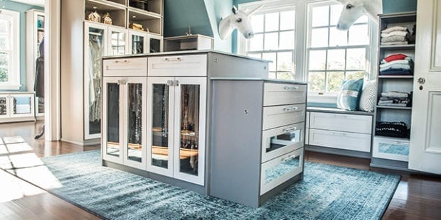 Walk in closet with a center island, custom cabinets, drawers and bench seating created by California Closets