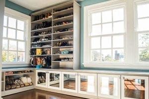 Custom shoe storage and shelving with glass front door cabinets in a light wood finish by California Closets