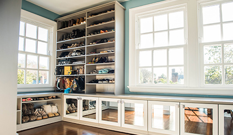 Custom shoe storage and shelving with glass front door cabinets in a light wood finish by California Closets