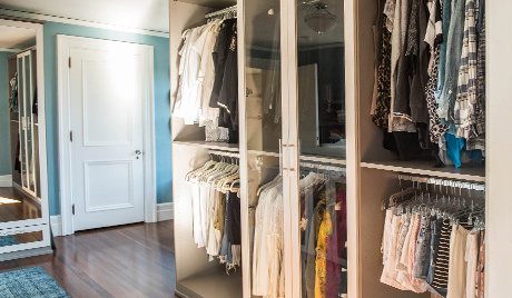 Organized clothes hanging behind glass doors in a custom walk in closet designed by California Closets