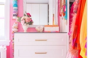 A white dresser surrounded by colorful hanging clothes and accessories