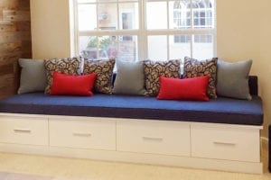 Window seat with white cabinet story underneath and a blue cushion with various pillows