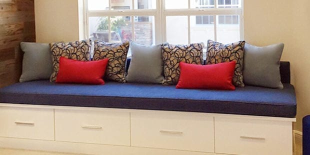 Window seat with white cabinet story underneath and a blue cushion with various pillows