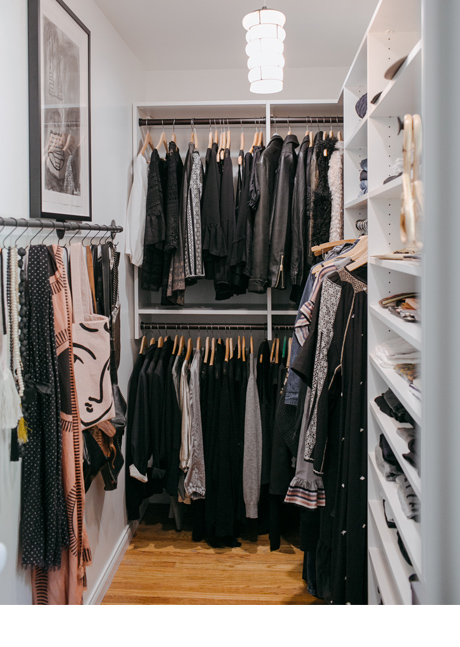 Narrow white walk in closet with dark clothes and accessories hanging up