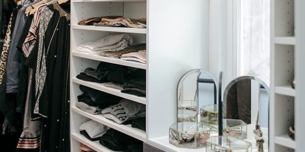 White shelves with folded clothes attached to a vanity with mirrors and glass jewelry boxes