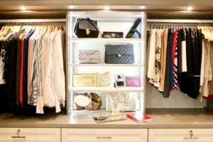 Organized clothes hanging and purses displayed in white shelving with LED lights