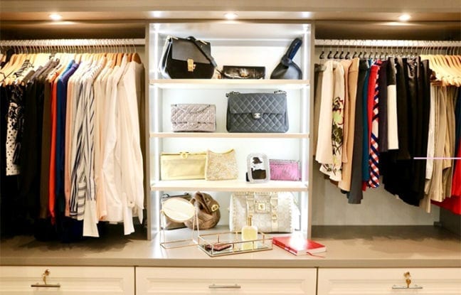 Organized clothes hanging and purses displayed in white shelving with LED lights