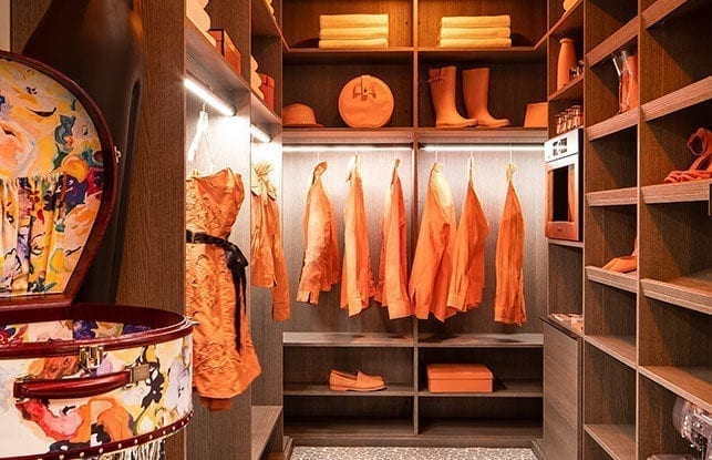 Walk in closet with wood finish and orange clothing and accessories hanging