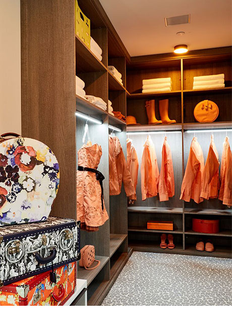 Left corner view of walk in closet with wood finish and orange clothe hanging