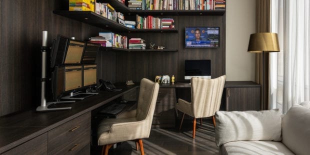 Dark wooden home office with two white chairs and 6 monitor display and book shelf