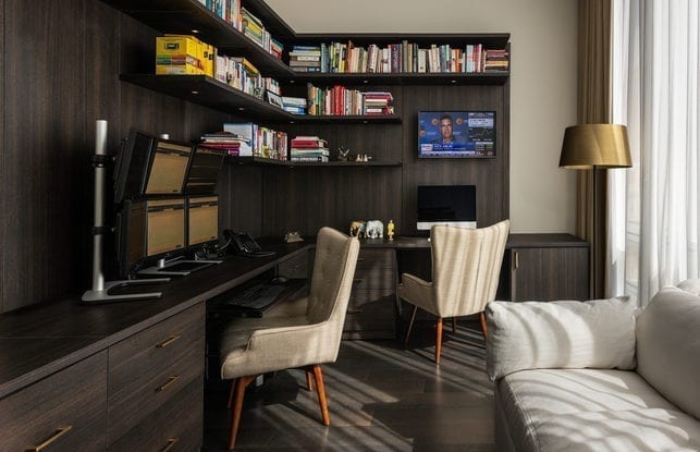 Dark wooden home office with two white chairs and 6 monitor display and book shelf