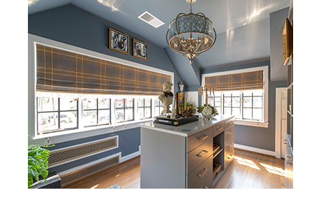 Blue walk-in closet with island dresser and light shining in through two wall windows designed by Amber Colo and Sarah Smith