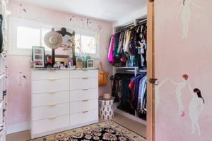 Pink walk in closet with white dresser with metal handles