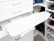Drawers with gold accents and fold-out ironing board in the white walk-in closet of influencer Kelly Natenshon