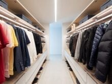 Narrow mens walk in closet with dark clothing hanging