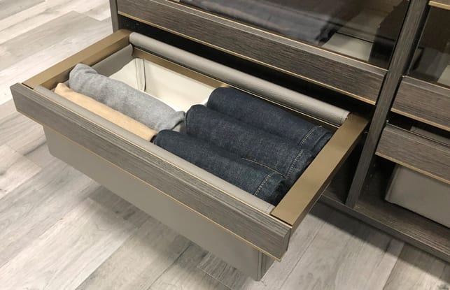 Custom drawer with baskets holding jeans and pants in a walk in closet in natural wood grain finish by California Closets