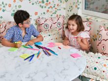 Two kids on white table with markers and floral walls