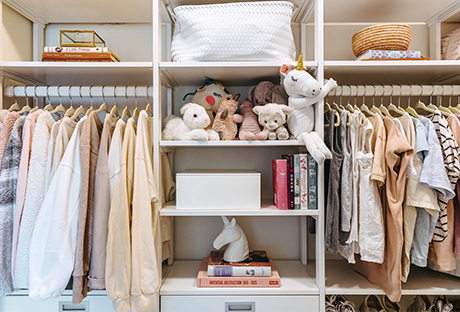 Custom white kids closet with two clothing rods and multiple cubbies with stuffed animals