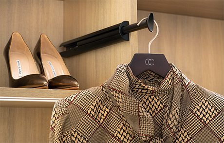 Camisa colgada en una barra de ropa en un armario con acabado de grano de madera, zapatos en un estante detrás de la prenda.