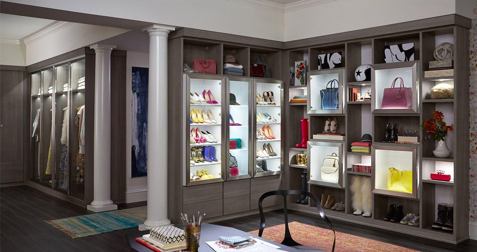 Walk in closet with a grey wood grain finish with accent lighting, shoe storage, drawers, and glass doors.