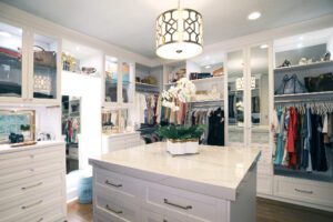 White luxury walk in closet designed in a custom layout with island in the center.