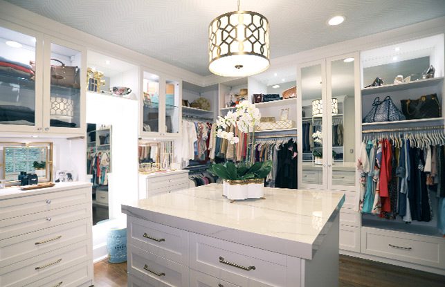 White luxury walk in closet designed in a custom layout with island in the center.