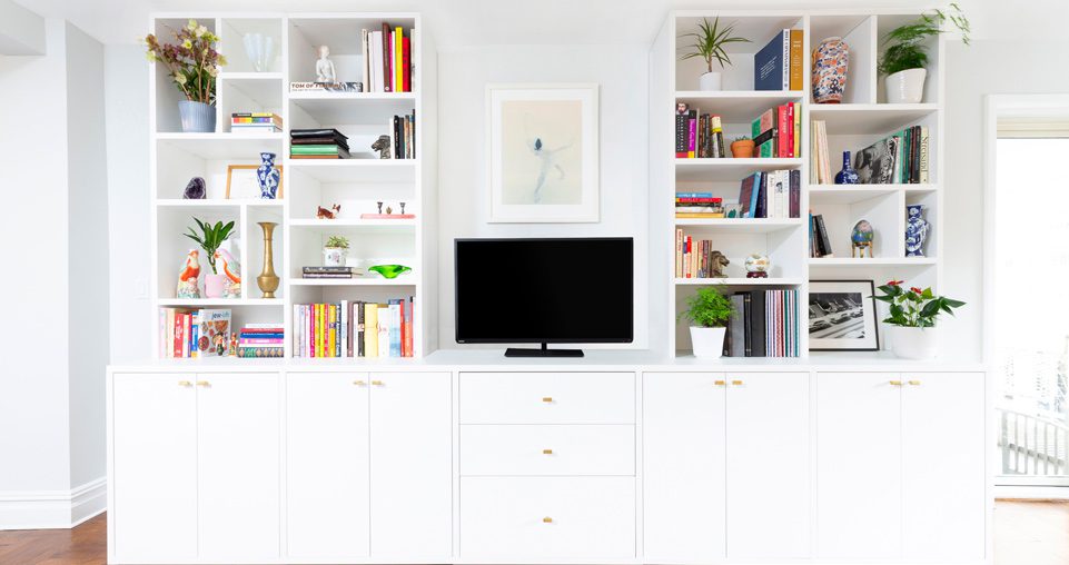 White media center with small tv on top, drawers and built in bookshelves to the left and right.