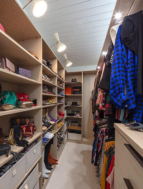 Walk in closet in light wood grain finish with custom shelves, shoe racks and drawers created by California Closets