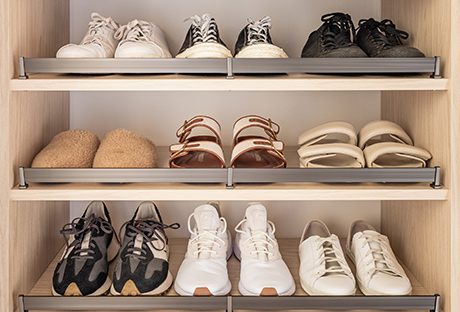 Shoe storage with metal shoe fence and tilted shelves in a custom walk in closet in a light wood grain finish by California Closets