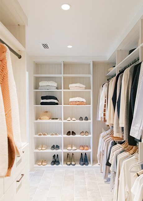 Custom walk in closet organization for sweaters, shoes and hanging clothes in a neutral wood grain finish by California Closets