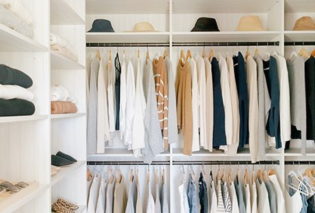 Walk in closet with custom shelving, shoe storage and hanging racks a in neutral wood grain finish by California Closets