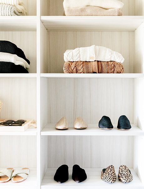 Walk in closet with custom shelving for shoes and sweaters in a neutral wood grain finish by California Closets