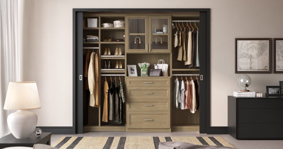 Reach in closet with built in cabinets and drawers and glass doors in medium grey wood grain finish by California Closets