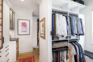 His closet is designed in a white wood grain finish with custom shelving and drawers created by California Closets