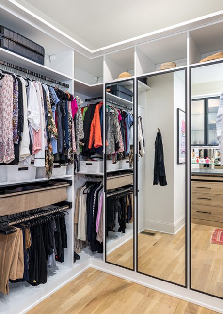 Her walk in closet with open shelves and mirrored doors in white wood grain finish created by California Closets