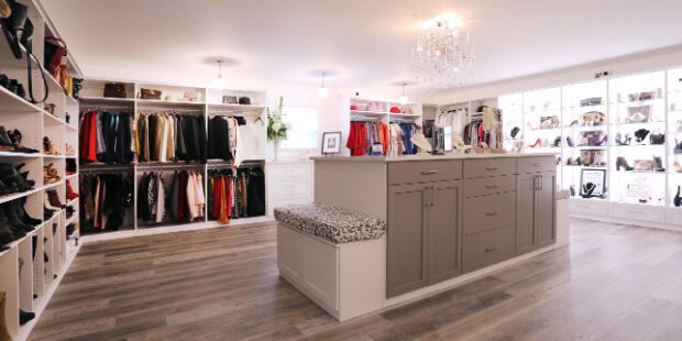 A walk in closet design with a boutique feel is designed with custom cabinets, drawers, LED lighting, shoe storage and a center island created by California Closets