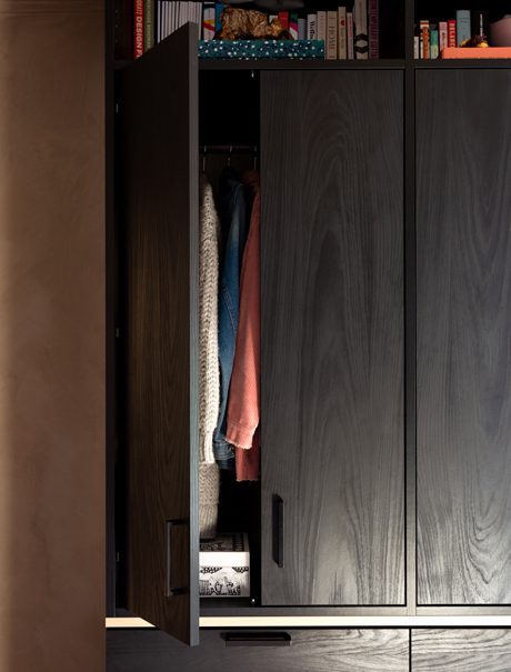 Puertas de armario abiertas para mostrar ropa con estantes para curiosidades arriba con acabado en madera veteada oscura de California Closets