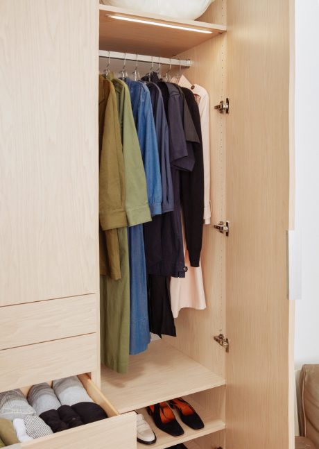 Wardrobe closet opened to show drawers and hanging clothes in a natural wood grain finish by California Closets