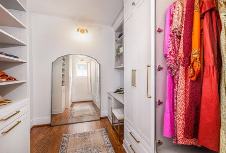 Custom walk in closet with built in open shelves, vanity and cabinets in light finish by California Closets
